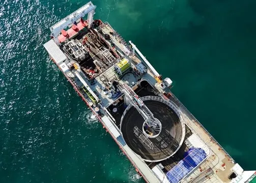 Aerial view of a cable-laying ship at sea with its cable carousel on deck